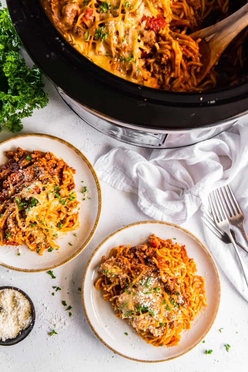 crockpot with spaghetti casserole and 2 plates with a serving of casserole on each