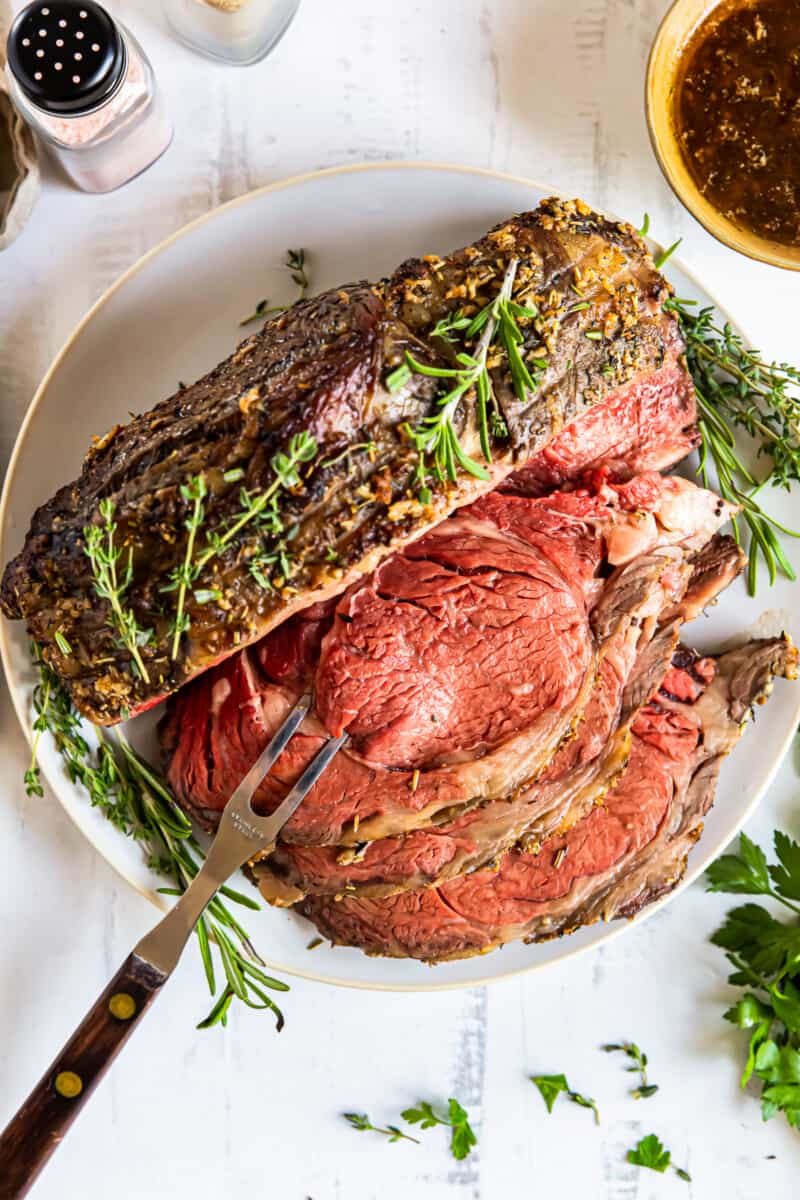 sliced garlic butter prime rib on a white plate with a serving fork