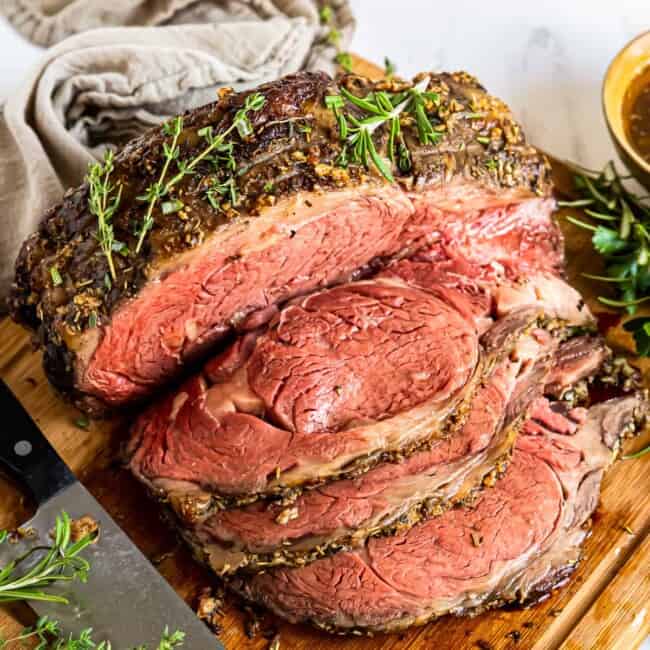 sliced garlic butter prime rib on a wood cutting board with a knife