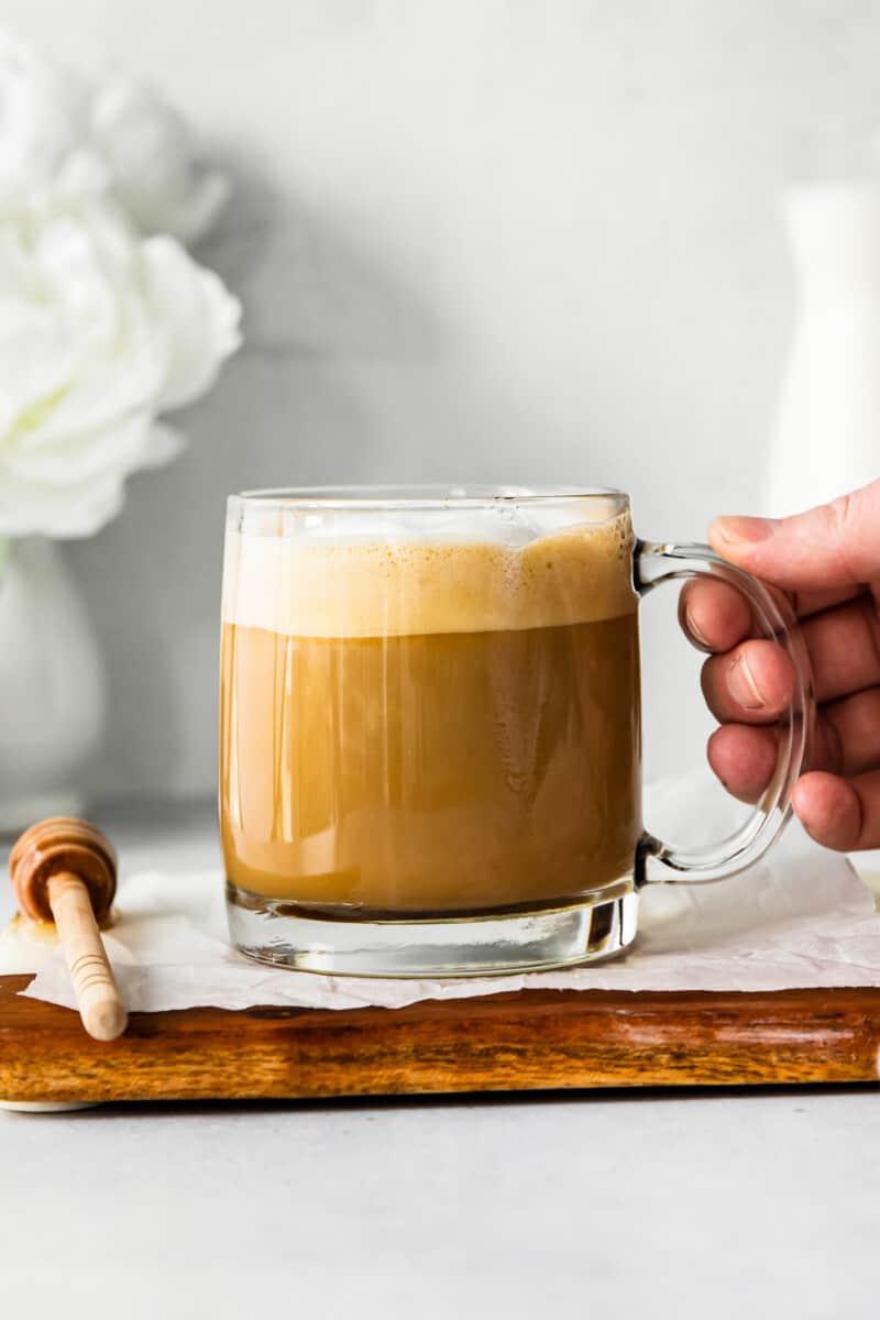hand holding a honey almond milk flat white in a clear glass mug