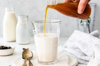 pouring apple syrup into clear glass of milk