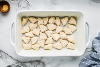 layer of cut up biscuit dough in the bottom of a white baking dish