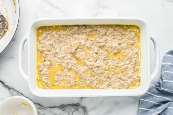 sausage gravy on top of cheese, egg mixture, and biscuit pieces in white baking dish before baking