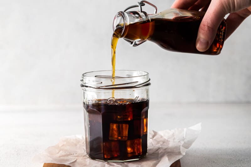 hand pouring brown sugar syrup into clear glass filled with ice and espresso