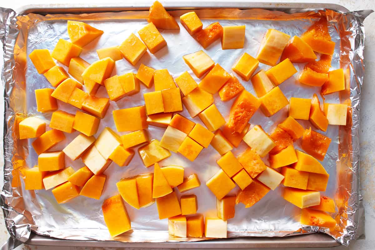 Cubes of butternut squash spread out on a lined baking sheet.