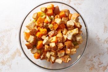 cubed bread added to butternut squash stuffing in a glass bowl.