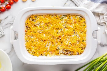assembled breakfast casserole with cheese on top in white shallow casserole dish before cooking