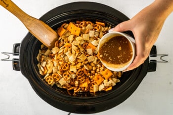 hand pouring butter sauce into chex mix in a crock pot