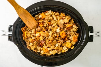 chex mix in a crock pot with a wooden spoon
