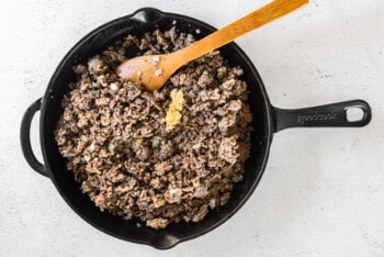 cooked ground beef, sausage, and onion in a skillet with a wood spoon