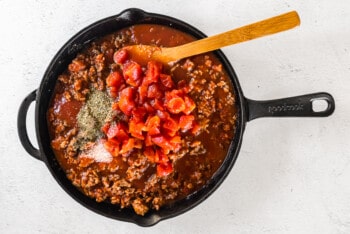meat sauce with diced tomatoes and spices in a skillet with a wood spoon