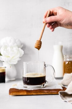 hand adding honey to espresso in a clear mug