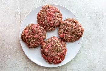 4 hamburger patties on a white plate before cooking
