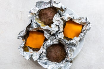 4 cooked hamburger patties with foil open and 2 are topped with slices of cheddar cheese