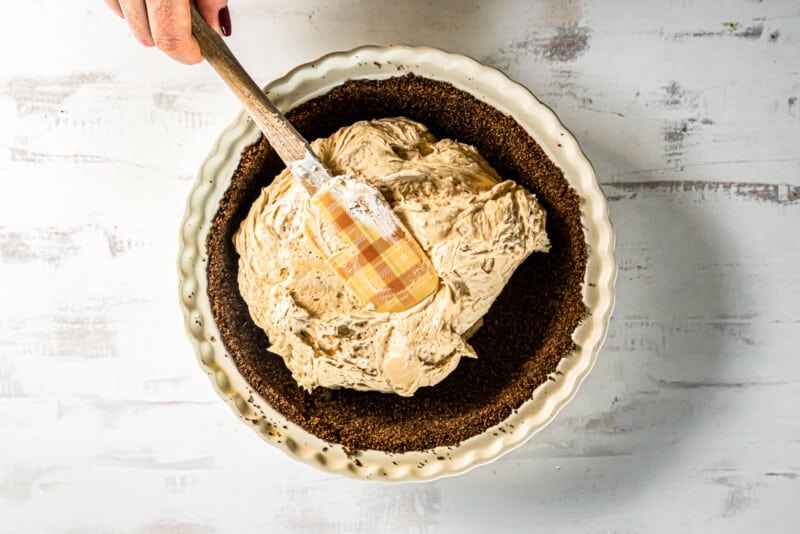 hand spreading peanut butter pie filling into pie dish with a spatula