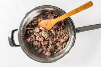 cooking breakfast sausage in a skillet with a wood spoon