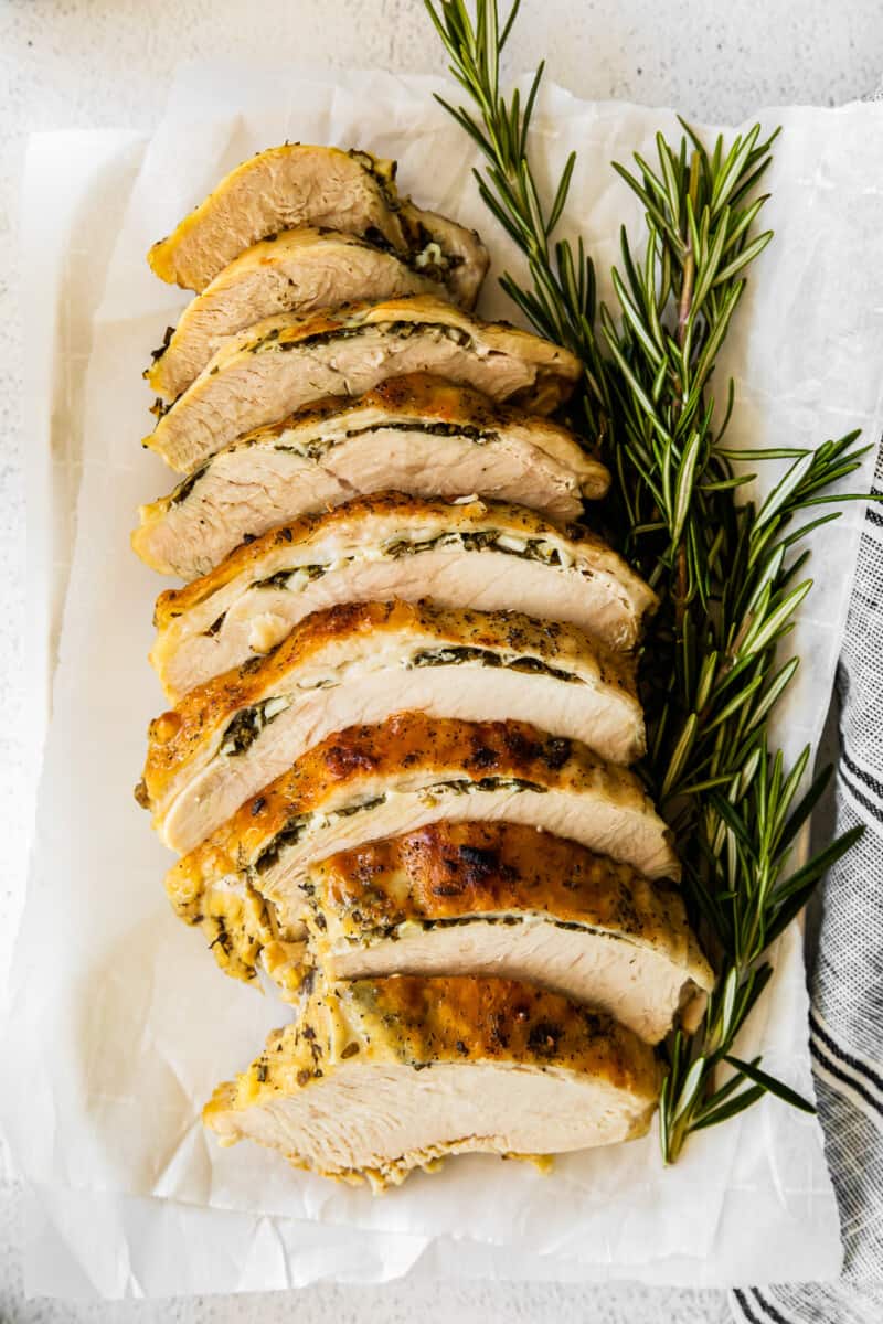 overhead image of garlic herb turkey breast sliced on a white platter with sprigs of fresh rosemary