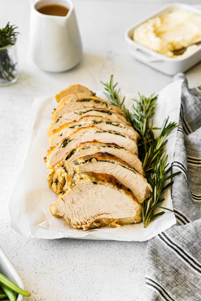 garlic herb turkey breast sliced on a white platter with sprigs of fresh rosemary