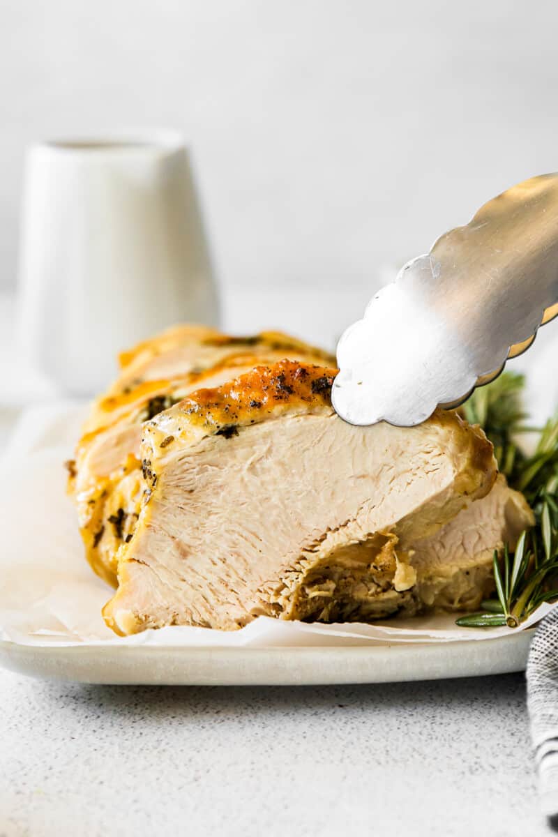 tongs grabbing a slice of garlic herb turkey off of a white platter