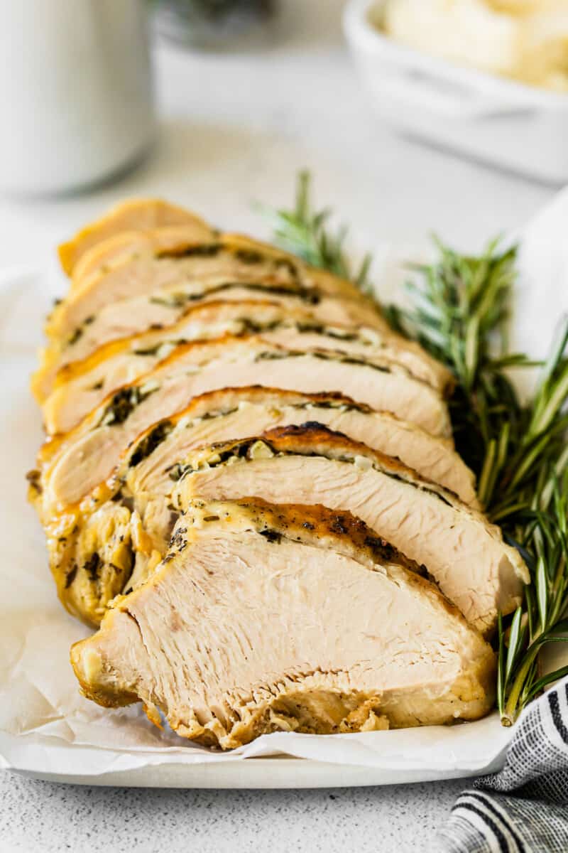 sliced garlic herb turkey breast sliced on a white platter with sprigs of fresh rosemary