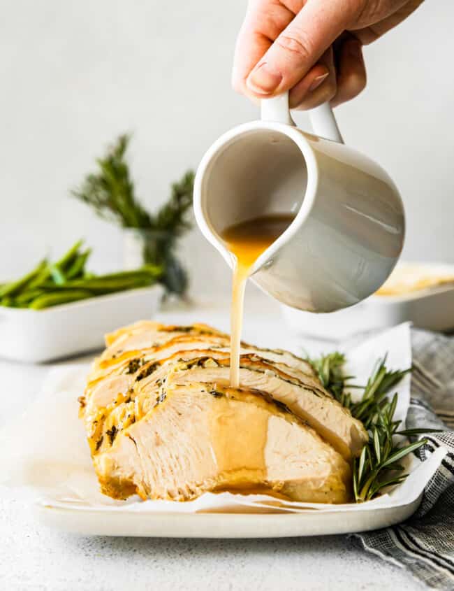 hand pouring gravy onto slices of garlic herb turkey breast