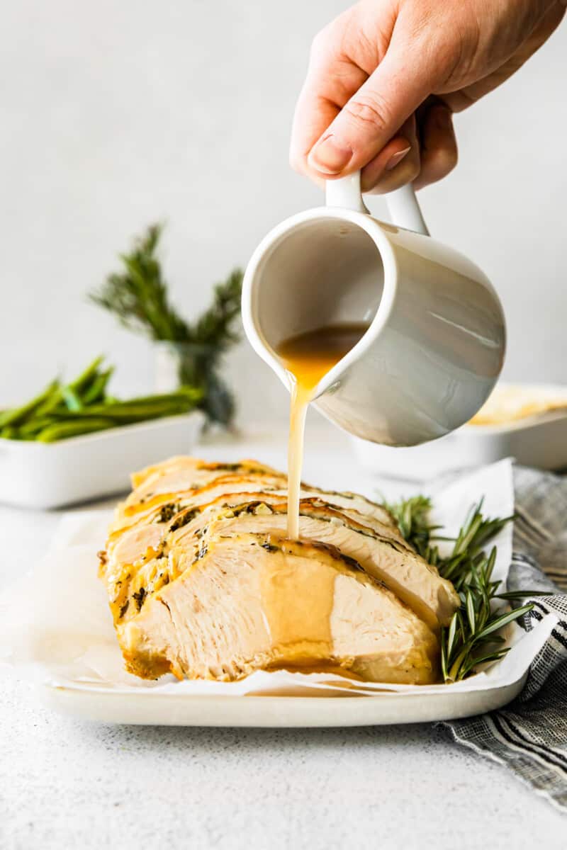 hand pouring gravy onto slices of garlic herb turkey breast