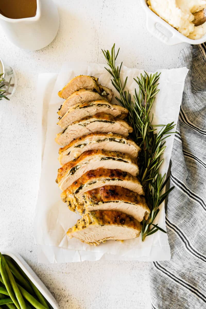 overhead image of garlic herb turkey breast sliced on a white platter with sprigs of fresh rosemary
