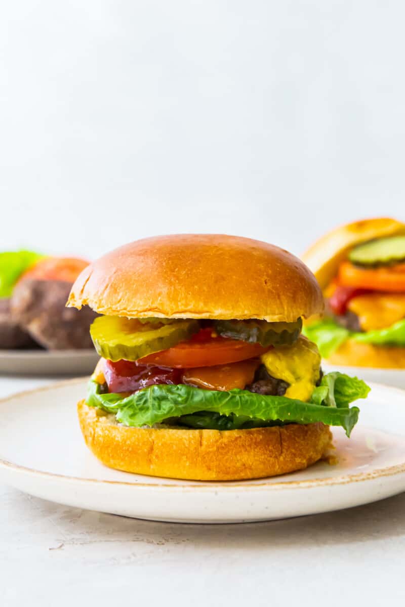 cheeseburger with a bun on a white plate topped with lettuce, cheese, ketchup, tomato slice, and pickles