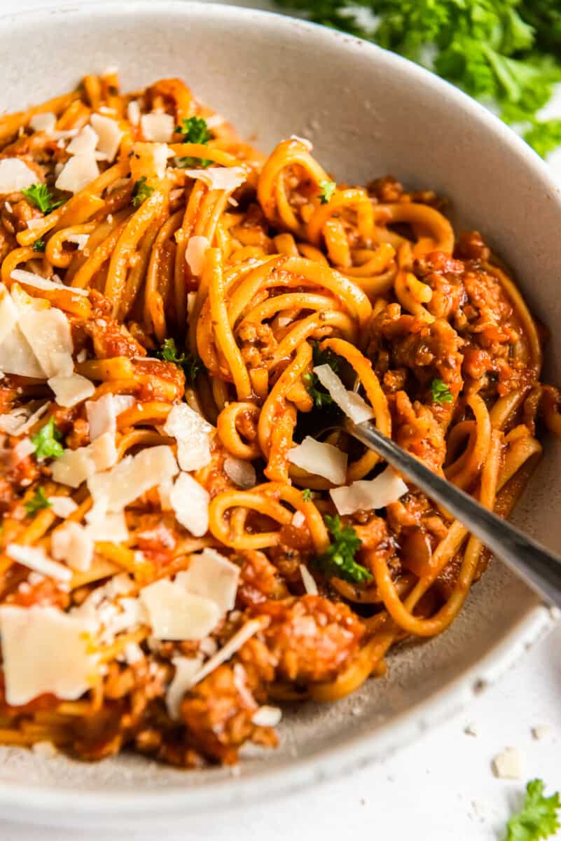 spaghetti topped with herbs and parmesan cheese in a white bowl with a fork