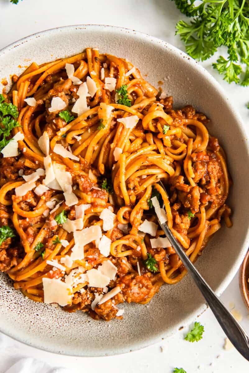 spaghetti topped with herbs and parmesan cheese in a white bowl with a fork