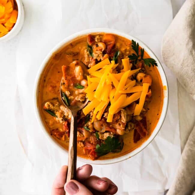 hand holding a spoon in a bowl of turkey white bean chili