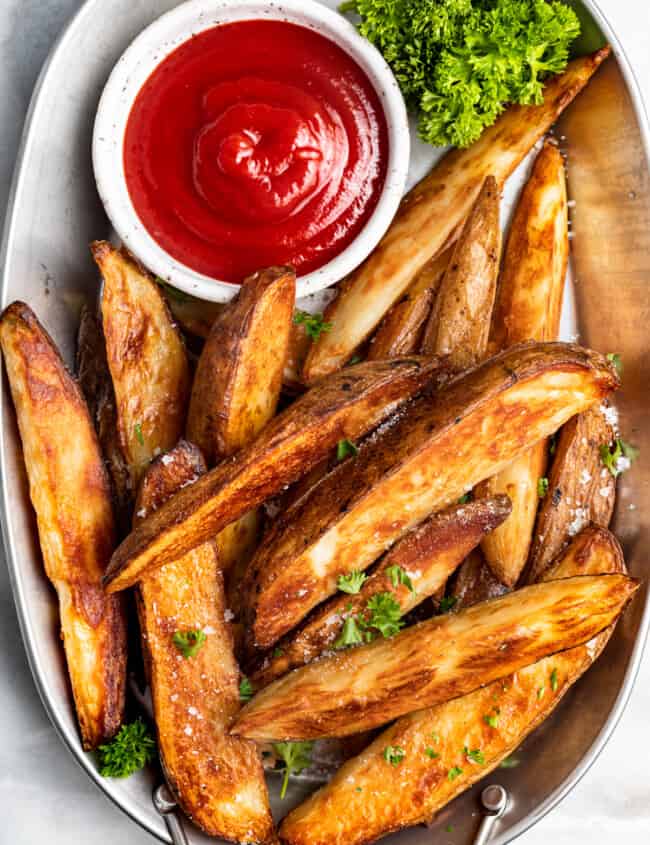 potato wedges on a white serving platter with ketchup in a white bowl