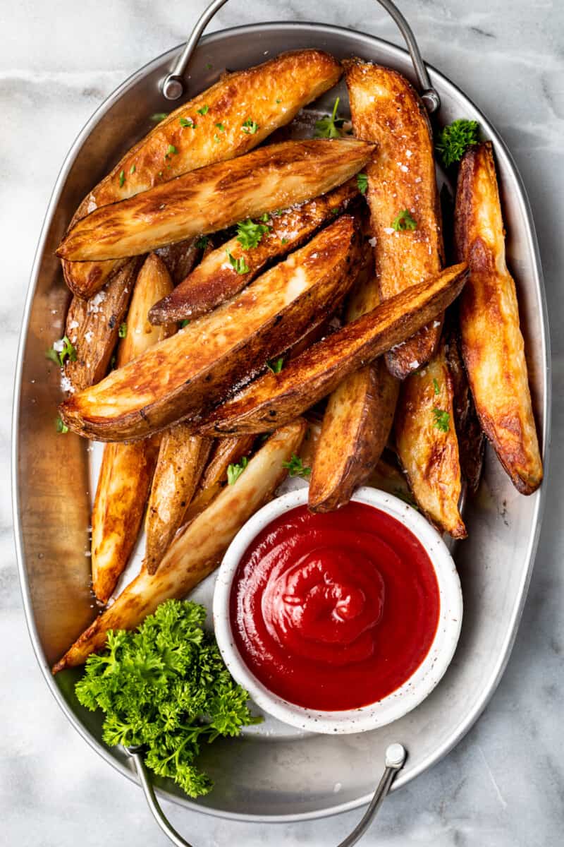 potato wedges on a white serving platter with ketchup in a white bowl