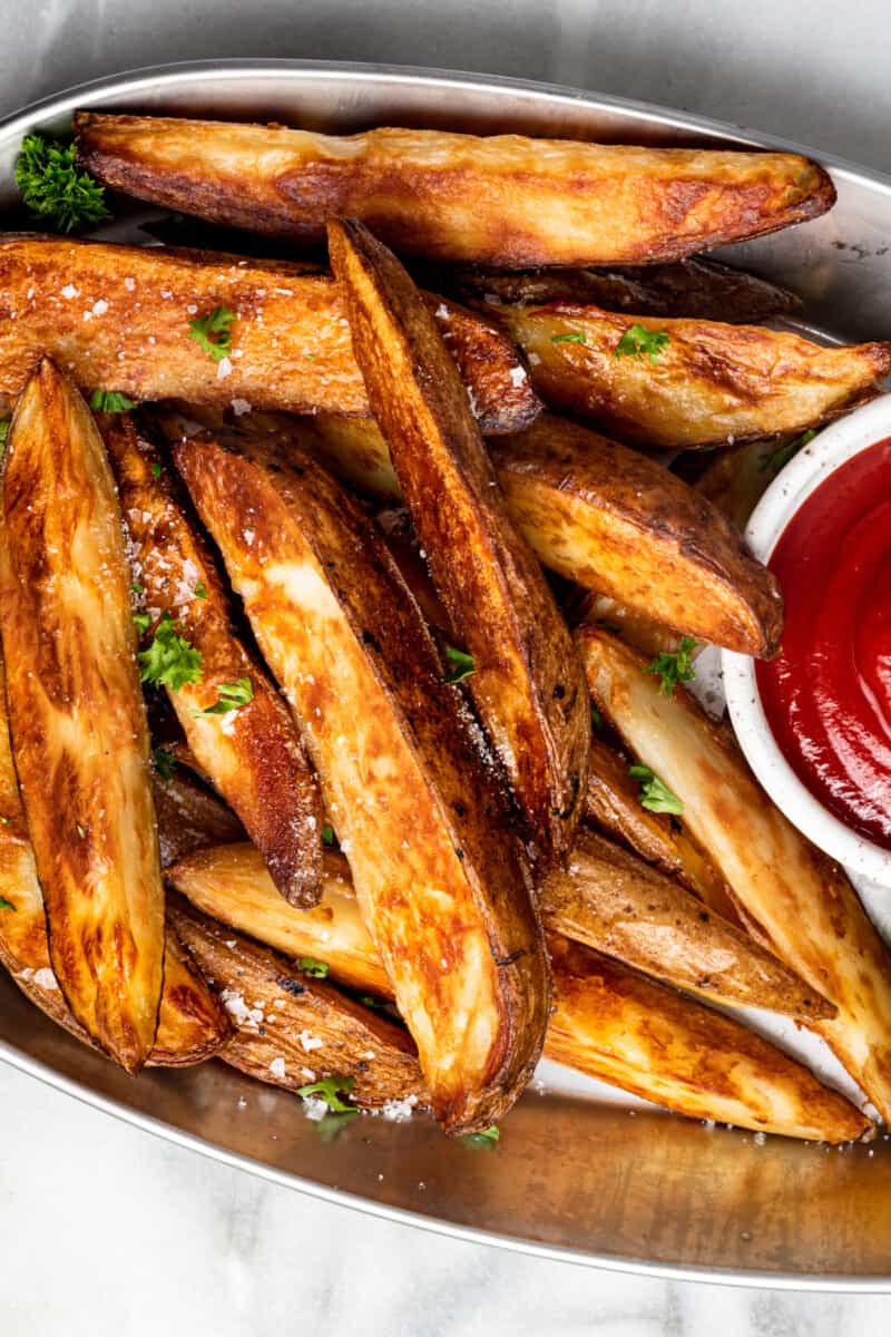 potato wedges on a white serving platter with ketchup in a white bowl