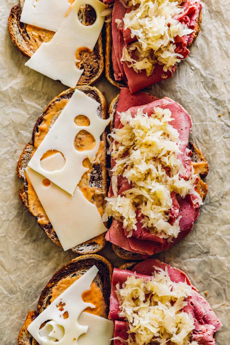 how to make classic reuben sandwiches, slices of rye bread topped with Swiss cheese, thousand island dressing, corned beef, and sauerkraut