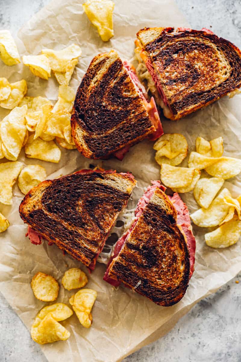 two Reubens on parchment paper surrounded by potato chips