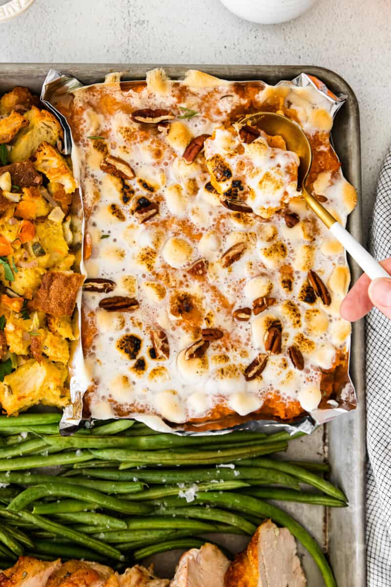 sweet potato casserole with marshmallows on a sheet pan with a hand holding a serving spoon