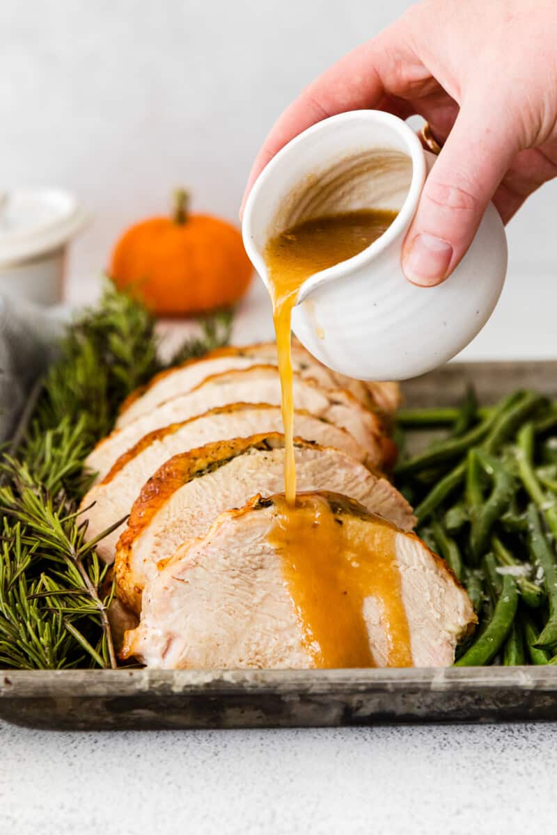 hand pouring gravy onto sliced turkey breast