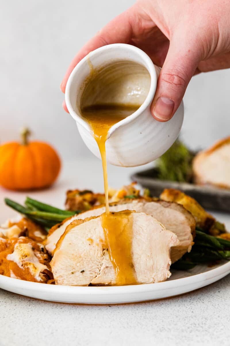 hand pouring gravy onto sliced turkey breast
