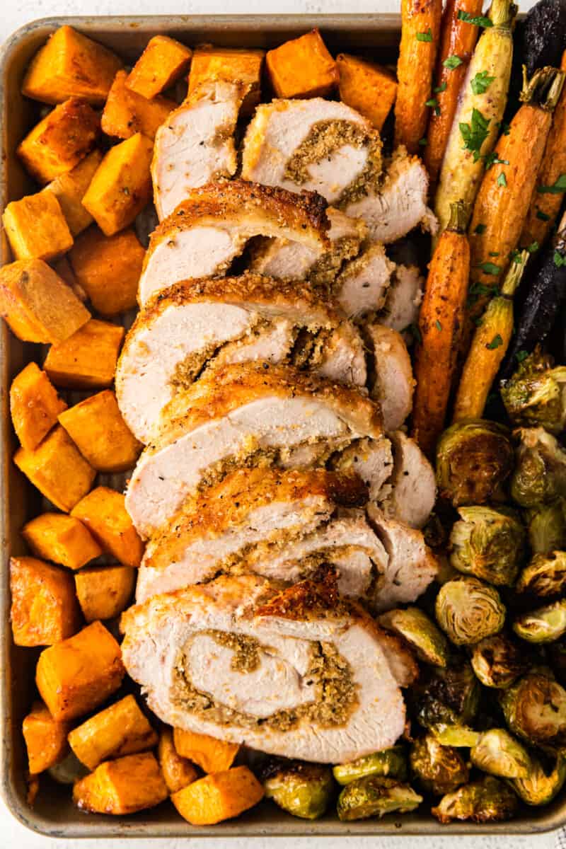 roasted sweet potatoes, carrots, and Brussels sprouts and sliced turkey roulade on a sheet pan