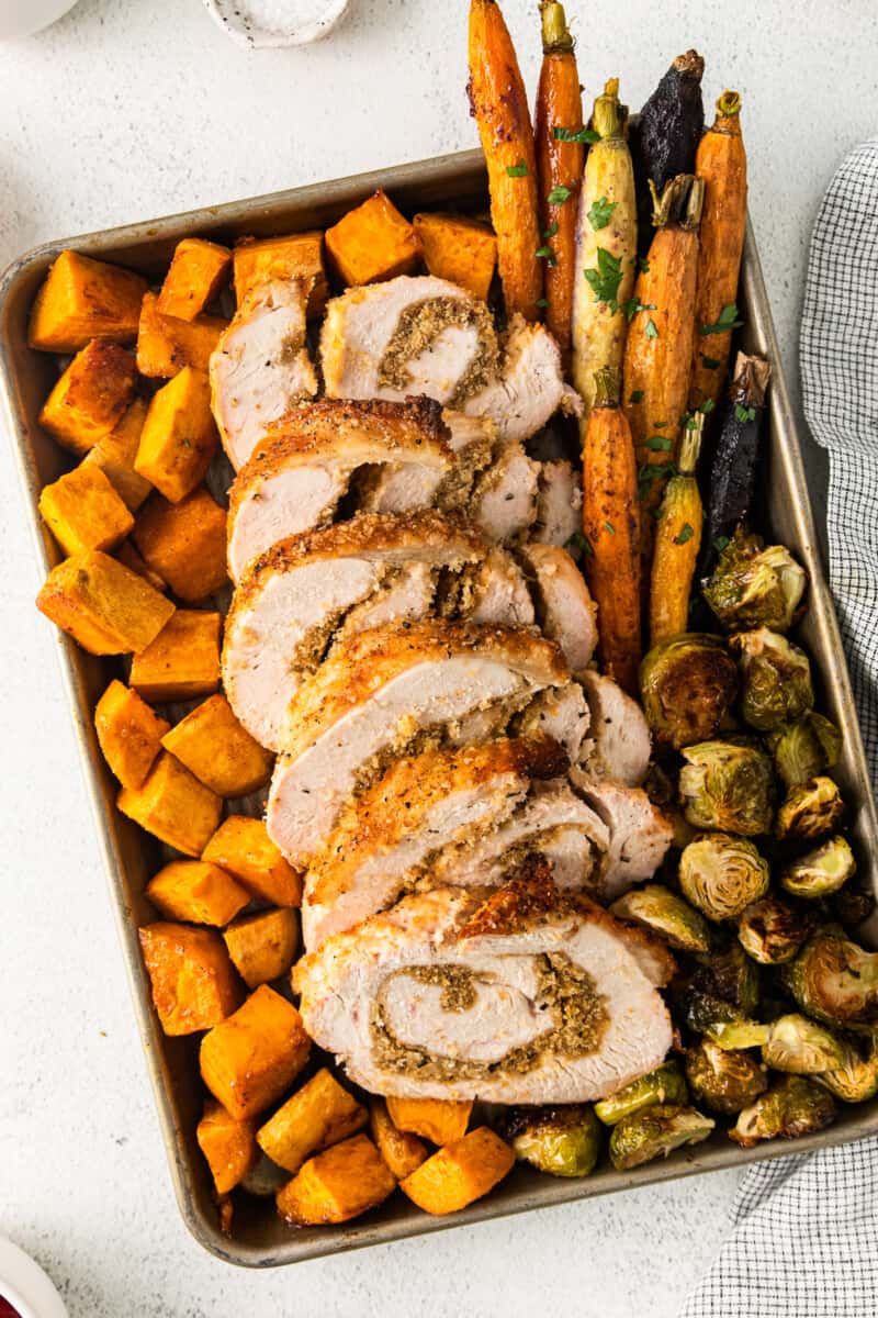 roasted sweet potatoes, carrots, and Brussels sprouts and sliced turkey roulade on a sheet pan