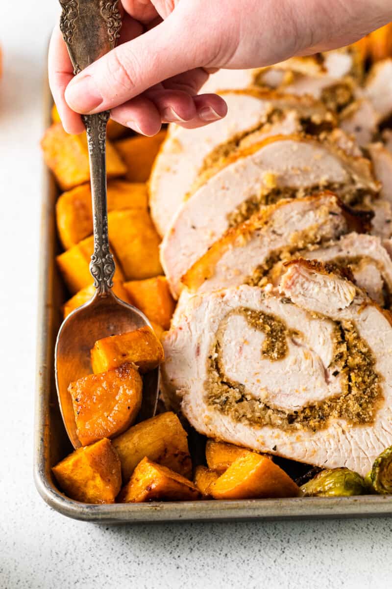 hand holding a spoon scooping up roasted sweet potatoes off of a baking sheet