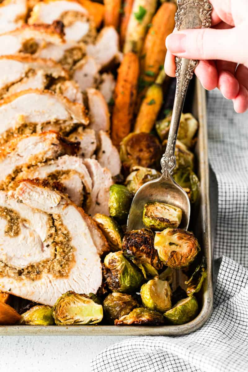 hand holding a spoon scooping up roasted Brussels sprouts off of a baking sheet