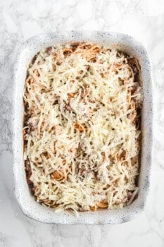 spaghetti mixture topped with cheese in a casserole pan before baking