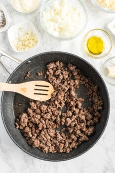 ground beef in a skillet with a wood spoon