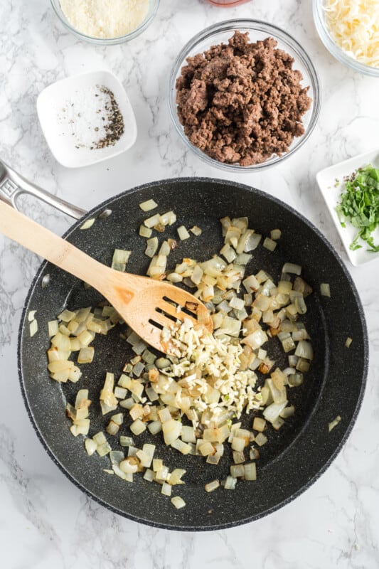 minced garlic and cooked chopped onions in a skillet with a wood spoon