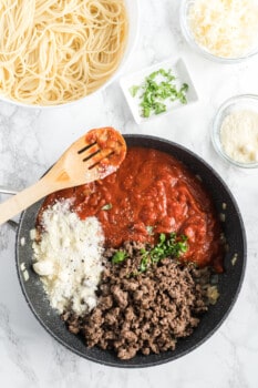 parmesan cheese, marinara sauce, and ground beef in a skillet with a wood spoon