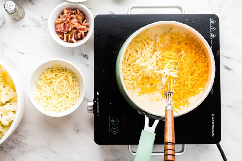 cheese added to loaded cauliflower bake sauce in a saucepan with a whisk.