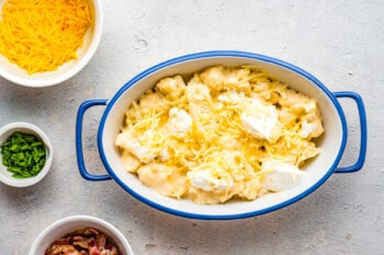 cheese and dollops of sour cream over loaded cauliflower in a blue and white casserole dish.