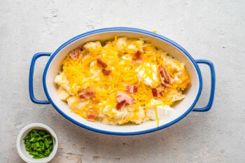 bacon and cheese added to loaded cauliflower in a blue and white casserole dish.
